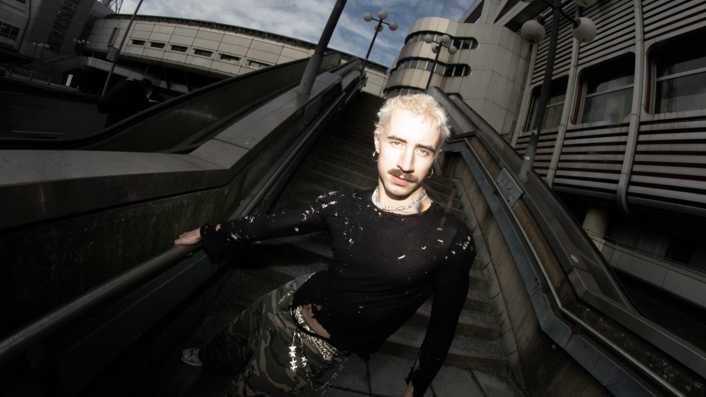 Melvin Hein on a concrete staircase, wide angle, in a ripped black top